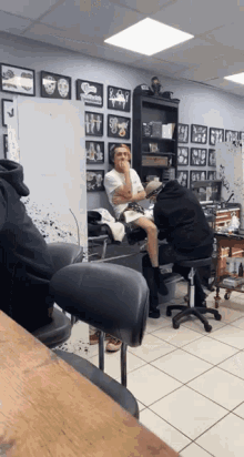 a man sits in a chair in a tattoo shop while another man sits behind him