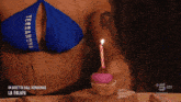 a woman in a bikini is holding a cupcake with a lit candle on it