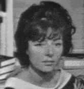 a black and white photo of a woman 's face with books in the background .
