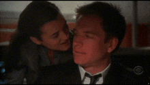 a woman is kissing a man on the cheek while he is wearing a suit and tie .