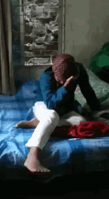 a man is sitting on a bed covering his face with his hands .