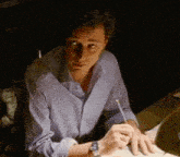 a man wearing a watch is sitting at a desk writing on a piece of paper