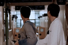 two men are standing next to each other in a hallway . one of the men is holding a camera .