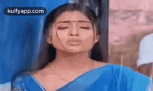 a woman in a blue saree is standing in front of a window with her eyes closed .