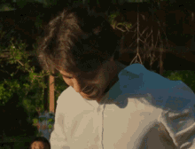 a man in a white shirt is standing in front of a tree .