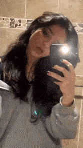 a woman is taking a selfie with her phone in a bathroom mirror .