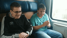 a boy wearing a umbro jacket sits next to another boy on a train