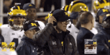 a man wearing a hat with the letter m on it is talking on a cell phone