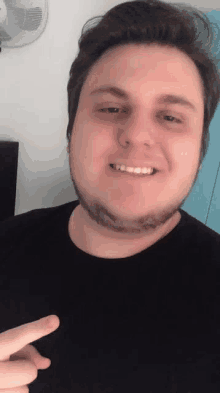 a man with a beard and a black shirt is smiling and pointing at the camera .