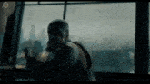 a man in a superhero costume is standing in front of a window holding a gun .