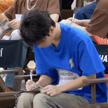 a man in a blue shirt with the name nguyen on it is writing on a piece of paper