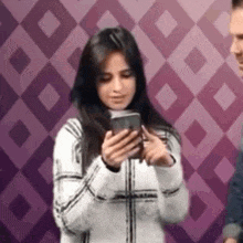 a woman is holding a cell phone in her hands in front of a purple wall .