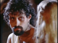 a man with a beard and earrings is looking at a woman with blonde hair .