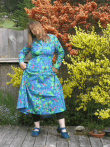 a woman in a blue and green floral dress stands on a deck