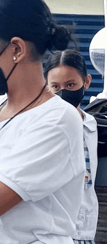 a woman wearing a black face mask stands next to another woman wearing a white shirt