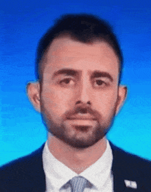 a man with a beard is wearing a suit and tie with a blue background