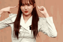 a young woman in a white jacket is making a funny face while pointing at her ears .