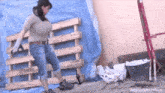 a woman with large breasts is standing in front of a wooden pallet holding a hammer .