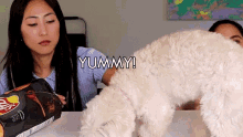 a woman holds a bag of chips next to a white dog and says yummy