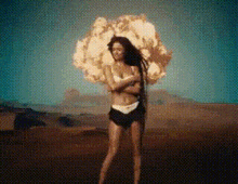 a woman in a bikini is standing in front of an exploding bomb .