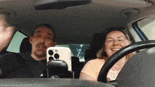 a man and a woman are sitting in a car with a cell phone in the back seat