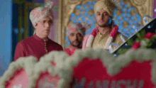 a group of men in turbans are standing in front of a sign that says ' manish ' on it .