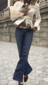 a woman in a white shirt and blue jeans is walking down a sidewalk