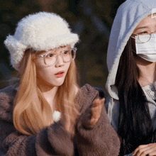 a woman wearing glasses and a white hat stands next to a woman wearing a mask