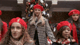 a group of girls wearing red hats with a treble clef on them are standing in front of a christmas tree