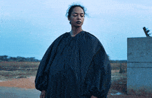 a woman wearing a black dress with balloon sleeves stands in a field
