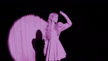 a woman with pink hair is standing in front of a pink curtain in a purple dress .