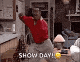 a man is dancing in a living room with the words `` show day '' written on the screen .