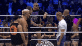 a group of men are standing in a ring with a aew logo on the wall behind them
