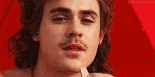 a close up of a man 's face with a mustache holding a piece of paper in his hand .