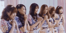 a group of girls are standing in a row with their hands folded in front of their faces