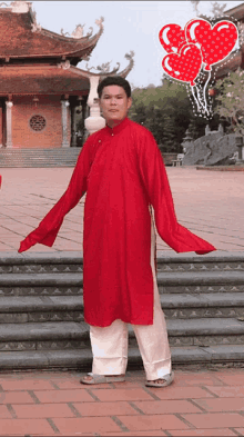 a man in a red shirt and white pants stands in front of a temple