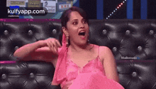 a woman in a pink dress is sitting on a couch with her mouth open .
