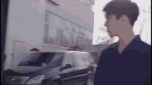 a man in a blue shirt is walking in front of a car .