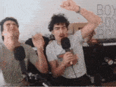 two men are singing into microphones in front of a wall that says boy boy boy