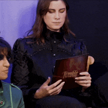 a woman in a black shirt is reading a book called trouble brewing