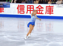 a woman in a blue dress is ice skating in front of a sign that says live on it