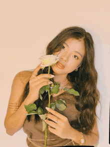 a woman in a brown top is holding a white rose in her hand