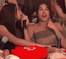 a woman singing into a microphone while sitting on a red pillow with the letter s on it .