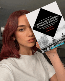 a woman with red hair holds a book titled adapting to transform networked conflict