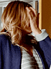 a woman covering her face with her hands while wearing a striped shirt and a blue jacket