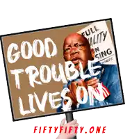 a hand holds up a sign that says " good trouble lives on "
