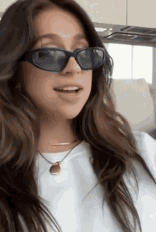 a woman wearing sunglasses and a white t-shirt is sitting on a couch .