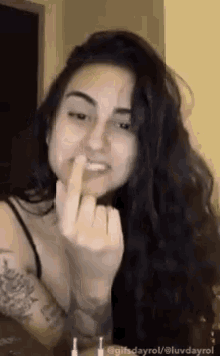 a woman is giving the middle finger to the camera while holding her finger to her mouth .