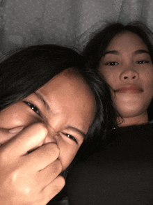 two girls are making funny faces and one is covering her nose with her hand