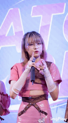 a girl in a pink outfit holds a microphone in front of a sign that says at